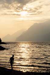 Italy, Veneto, Malcesine, Boy standing at Lake Garda in evening light - LVF002168