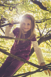 Portrait of smiling little girl climbing in an autumnal tree - SARF001020