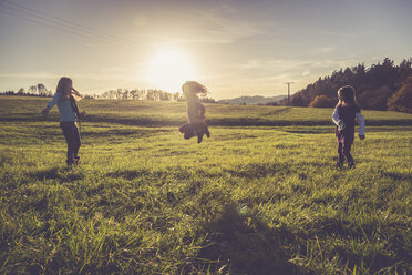 Three little girls playing with a spiral on a meadow in backlight - SARF001015