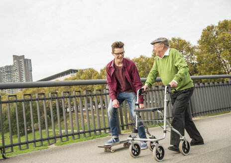 Glücklicher älterer Mann mit Rollator und erwachsenem Enkel mit Skateboard - UUF002648