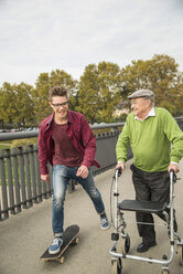 Happy senior man with wheeled walker and adult grandson with skateboard - UUF002649