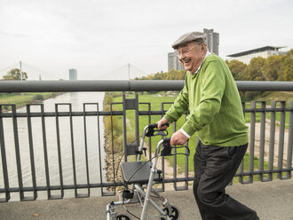 Verspielter älterer Mann mit Rollator auf einer Brücke - UUF002652