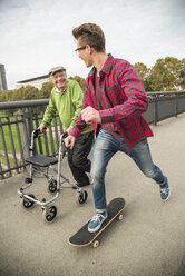 Glücklicher älterer Mann mit Rollator und erwachsenem Enkel mit Skateboard - UUF002653