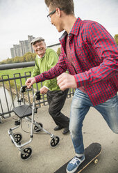 Glücklicher älterer Mann mit Rollator und erwachsenem Enkel mit Skateboard - UUF002654