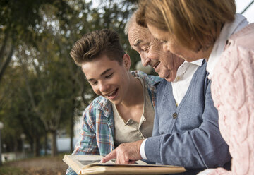 Älterer Mann mit Enkel und Tochter beim Betrachten eines Fotoalbums - UUF002671