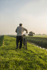 Senior man in rural landscape pushing bicycle - UUF002692