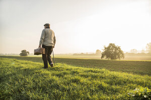 Älterer Mann mit Tasche beim Spaziergang in ländlicher Landschaft - UUF002731