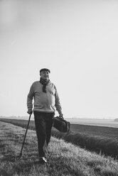 Älterer Mann mit Tasche beim Spaziergang in ländlicher Landschaft - UUF002697
