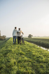 Älterer Mann und Enkel in ländlicher Landschaft mit Fahrrad - UUF002699