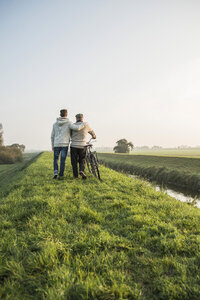 Älterer Mann und Enkel in ländlicher Landschaft mit Fahrrad - UUF002699