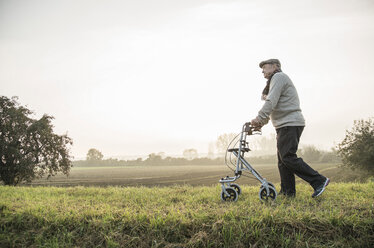 Älterer Mann mit Rollator zu Fuß in ländlicher Landschaft - UUF002705