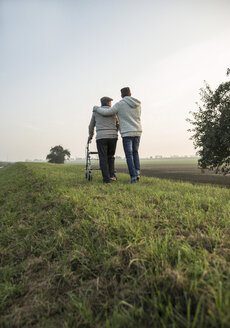 Senior man and grandson in rural landscape with wheeled walker - UUF002707