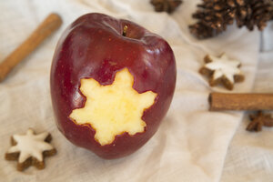 Roter Apfel mit sternförmigem Loch, Zimtsterne, Zimtstangen und Tannenzapfen auf Tuch - SARF001028