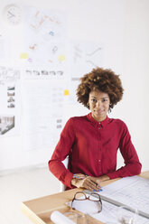 Portrait of smiling young female architect sitting at her desk - EBSF000332