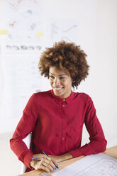 Smiling young female architect sitting at her desk - EBSF000333