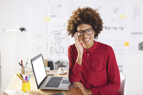 Porträt einer lächelnden jungen Architektin mit Laptop an ihrem Schreibtisch, lizenzfreies Stockfoto