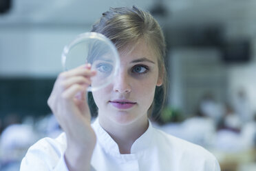 Young female natural scientist watching bacteria culture in petri dish at microbiology laboratory - SGF001016
