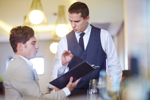 Geschäftsmann gibt eine Bestellung bei einem Kellner im Hotelrestaurant auf, lizenzfreies Stockfoto