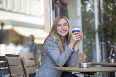 Lächelnde junge Frauen sitzen in einem Straßencafé mit Kaffee zum Mitnehmen - SHKF000025