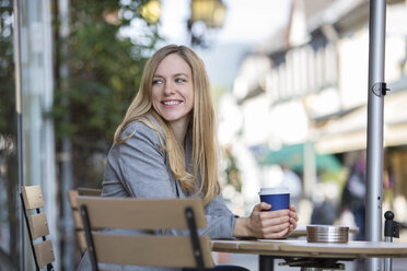 Lächelnde junge Frauen sitzen in einem Straßencafé mit Kaffee zum Mitnehmen - SHKF000026