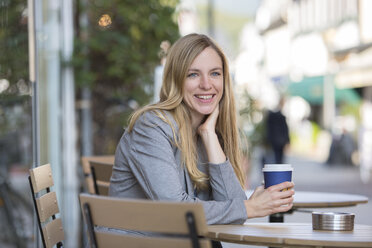 Lächelnde junge Frauen sitzen in einem Straßencafé mit Kaffee zum Mitnehmen - SHKF000027