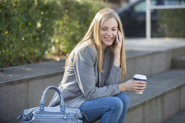 Smiling young women sitting at steps with coffee to go telephoning with smartphone - SHKF000032