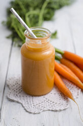 Glass of carrot smoothie and bunch of carrots on doily and white wood - ODF000869