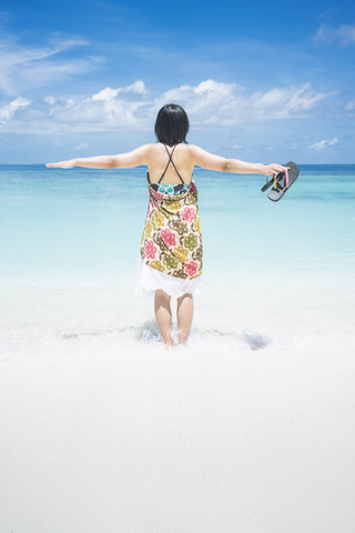 Malediven, Ari-Atoll, junge Frau mit ausgestreckten Armen im Wasser stehend am Meeresufer, lizenzfreies Stockfoto