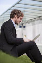 Geschäftsmann sitzt auf einer Wiese mit seinem digitalen Tablet - RBF002059