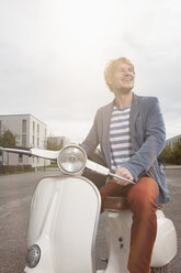 Lächelnder Mann sitzt auf seinem Motorroller im Gegenlicht - RBF002066