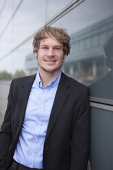 Portrait of smiling businessman in front of glass facade - RBF002068