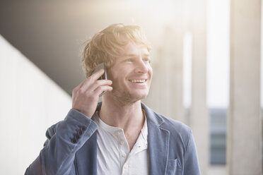 Portrait of smiling man telephoning with smartphone at backlight - RBF002075