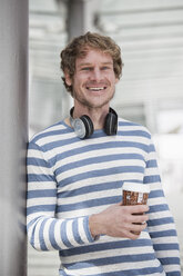 Porträt eines lächelnden Mannes mit Kopfhörern und Kaffee zum Mitnehmen - RBF002081