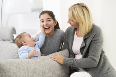 Mother sitting with daughter and baby boy on couch, smiling - GDF000591