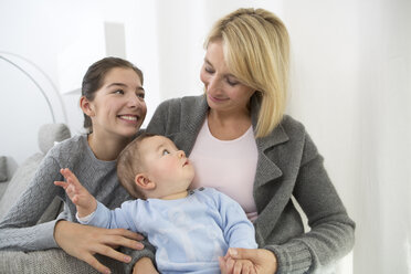 Mother sitting with daughter and baby boy on couch, smiling - GDF000592