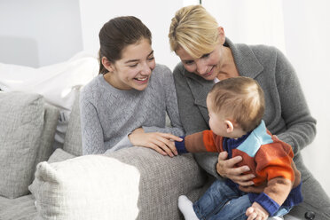Mutter sitzt mit Tochter und kleinem Jungen auf der Couch und lächelt - GDF000594