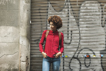 Smiling young woman standing in front of roller shutter with graffiti - EBSF000370