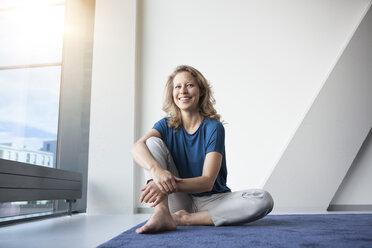 Portrait of smiling mature woman sitting on the floor at her apartment - RBF002032
