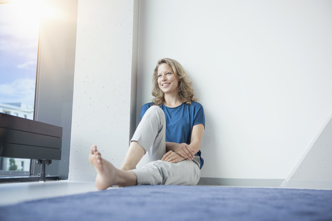 Porträt einer lächelnden reifen Frau, die in ihrer Wohnung auf dem Boden sitzt, lizenzfreies Stockfoto