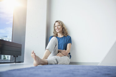 Porträt einer lächelnden reifen Frau, die in ihrer Wohnung auf dem Boden sitzt - RBF002035