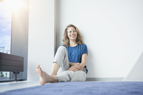 Porträt einer lächelnden reifen Frau, die in ihrer Wohnung auf dem Boden sitzt, lizenzfreies Stockfoto