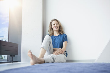 Portrait of smiling mature woman sitting on the floor in her apartment - RBF002036