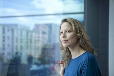 Porträt einer reifen Frau, die durch ein Fenster auf ihre Wohnung blickt - RBF002039