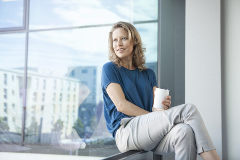 Lächelnde reife Frau schaut durch das Fenster auf ihre Wohnung - RBF002044