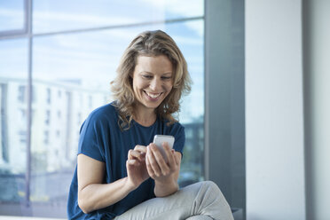 Smiling mature woman using her smartphone at home - RBF002046