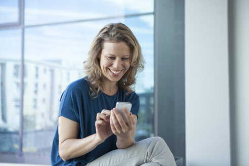 Lächelnde reife Frau, die ihr Smartphone zu Hause benutzt - RBF002046