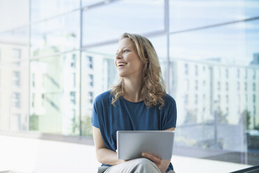 Smiling mature woman with digital tablet sitting in her apartment - RBF002048