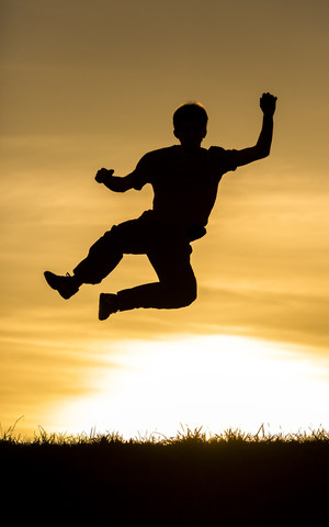 Silhouette eines springenden Mannes bei Sonnenuntergang, lizenzfreies Stockfoto