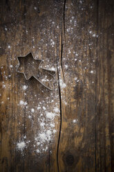 Cookie cutter shaped like a comet and scattered flour on dark wood - LVF002294