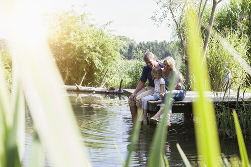 Glückliche Familie auf einem Steg am See sitzend - RBF001960